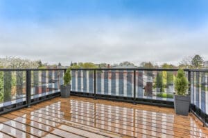 Spacious balcony with wooden flooring and modern railing overlooking a suburban neighborhood.