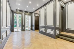 Elegant empty room with classic wall paneling and wooden herringbone flooring.