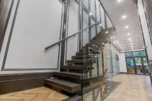 Modern floating staircase with glass railing and metal handrail.