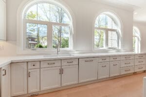 Bright kitchen with white cabinets and large arched windows.