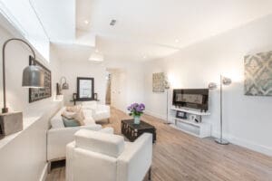 Bright, modern living room with white furniture and wooden flooring.