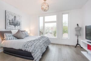 Bright modern bedroom with large windows and cozy gray bedding.