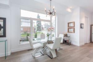 Modern dining room with glass table and white chairs by large windows.