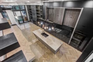 Modern kitchen with marble island and black cabinets under pendant lights.