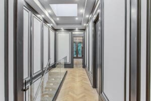 Elegant hallway with gray paneled walls and wooden herringbone floor.
