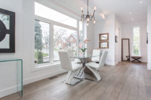 Bright dining area with white chairs and a glass table by large windows.