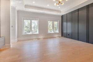 Bright, empty room with large windows and built-in dark wardrobes.