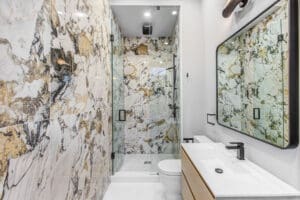 Modern bathroom with marble-patterned walls and glass shower enclosure.