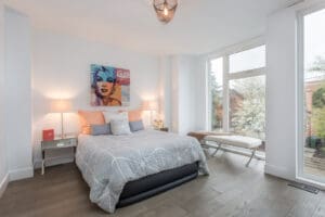 Bright bedroom with artistic wall decor and large windows.