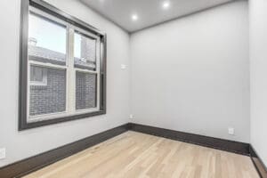 Empty modern room with light wood flooring and a large window.