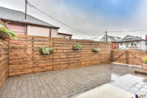 Wooden fence with small plants on a rainy day in a residential area.