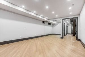 Empty room with white walls and wooden floor under bright ceiling lights.