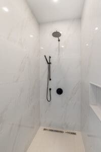 Minimalist white marble shower with black fixtures and built-in shelf.