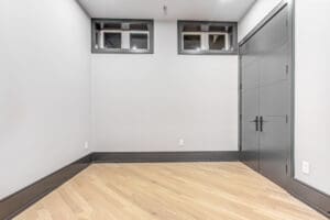 Empty room with white walls, small windows, and wooden floor.