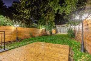 Cozy backyard with wooden deck, green lawn, and ambient lighting at night.