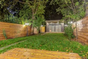 Well-lit backyard with green lawn and wooden deck at night.