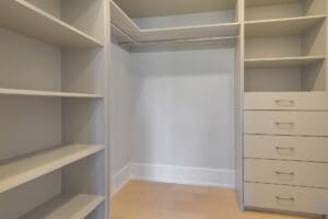 Empty walk-in closet with white shelves and drawers.