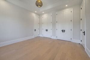 Empty room with three white doors and wooden floor.