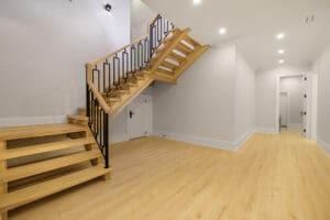 Modern wooden staircase with black metal railing in a minimalist room.