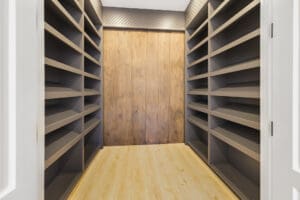 Empty wooden shelves lining a narrow room with a wooden floor and door.