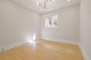Empty room with light wood flooring and a modern ceiling light fixture.