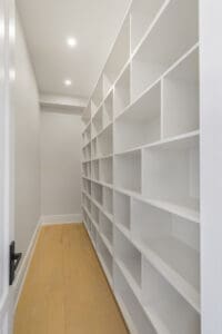 Empty white shelving units lining a narrow hallway with wooden flooring.