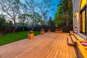 Spacious wooden deck with potted plants and lush green lawn at dusk.