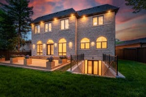 Modern brick house with warm lighting at dusk and spacious patio.