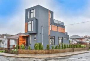 Modern three-story house with gray and wood panel exterior on a corner lot.