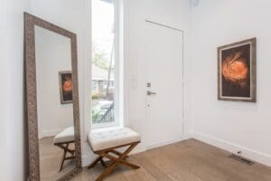 Minimalist entryway with a mirror, cushioned stools, and a closed white door.