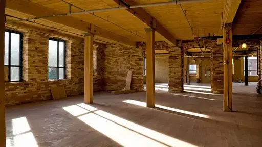 Sunlight streams through windows into an empty room with stone walls and wooden beams.